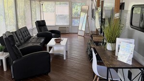 Un espacio al aire libre techado con un sofá de cuero negro, una mesa de centro blanca y una mesa de comedor con sillas.