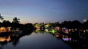 Una vía acuática tranquila con barcos, palmeras y edificios iluminados al anochecer.