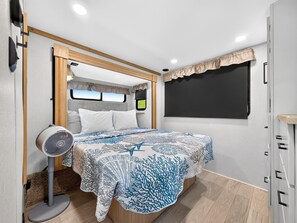 A compact RV bedroom with a bed, a fan, and a window. - Brand New 2025 RV 2BR + 2 Lofts, 2BA Pool & Marina (Key Largo)