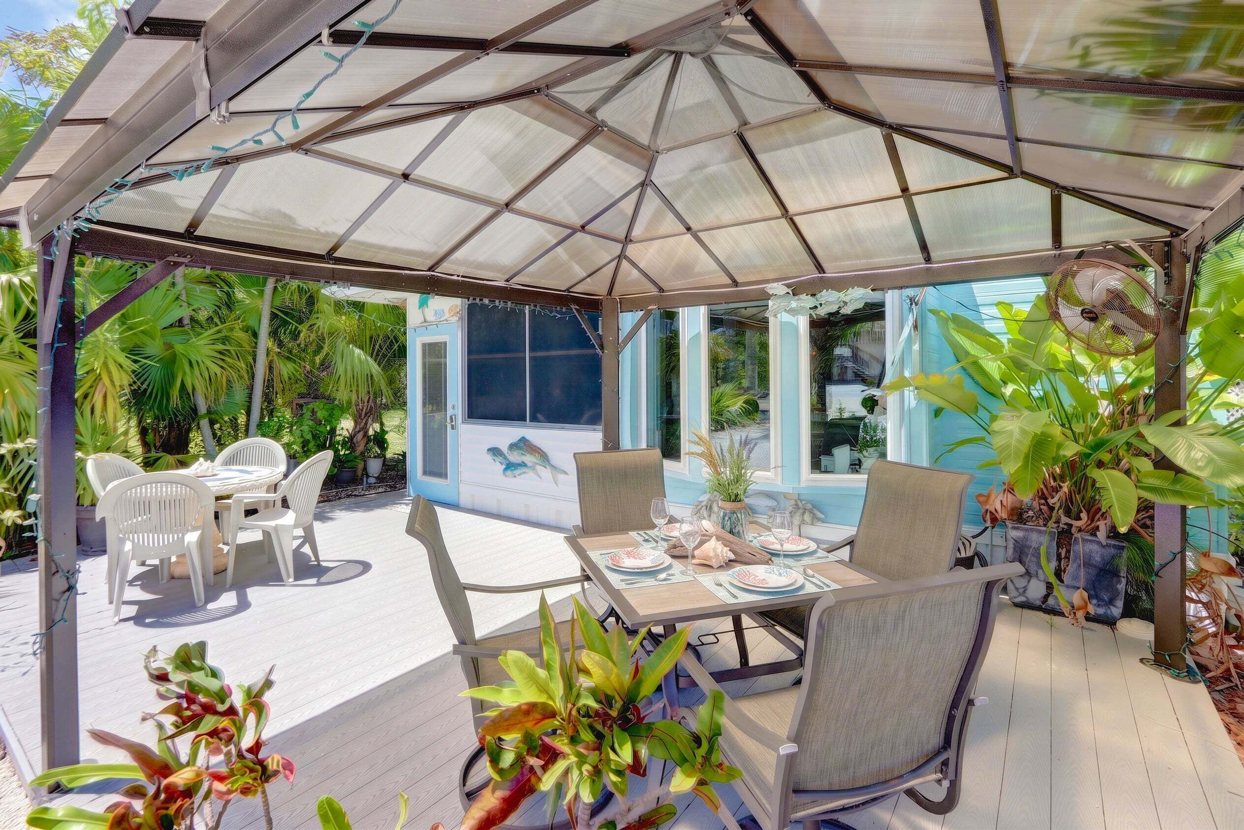 Une terrasse extérieure couverte, avec une table dressée pour les repas, entourée de chaises et agrémentée d’un ventilateur.