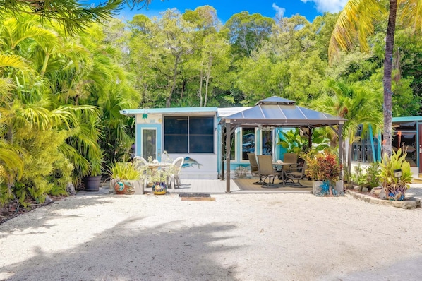 A small, modern house with a covered patio, surrounded by lush tropical vegetation.