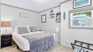 Une chambre à coucher comprenant un lit, une table de chevet, une lampe, des œuvres d’art murales et une fenêtre donnant sur un paysage.
