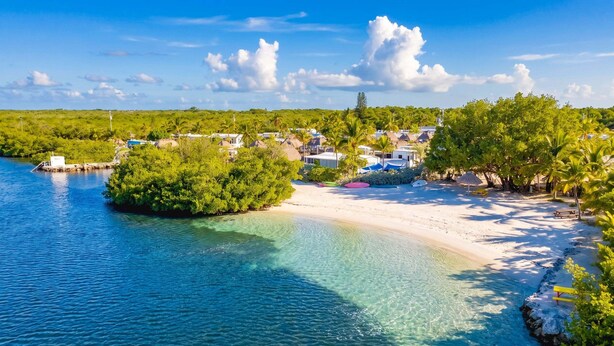 Zona costera con aguas cristalinas, una playa arenosa y una pequeña isla con edificios.