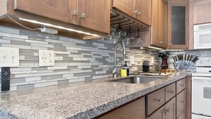 Una cocina con armarios de madera, encimera de granito, horno empotrado y salpicadero con azulejos grises.