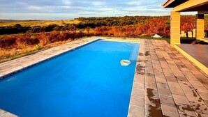 Una piscina rectangular con superficie de agua azul cristalina, rodeada por una solana con baldosas.