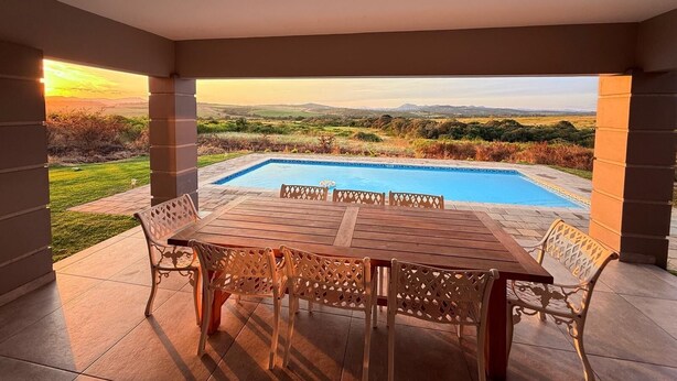 Un espacio al aire libre techado con piscina, una mesa y sillas.