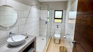 Un baño moderno con un espejo grande, un lavabo redondo, una cabina de ducha y un inodoro.