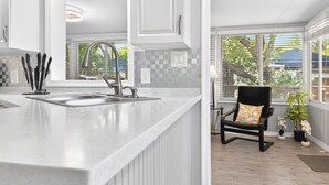 Une cuisine moderne dotée d’un grand îlot central, d’une chaise noire agrémentée d’un coussin coloré, et offrant une vue sur la verdure environnante.