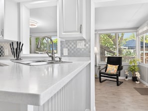 A modern kitchen with a large island, a black chair with a colorful cushion, and a view of greenery outside.