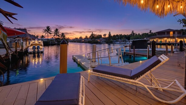 Une terrasse en bois avec des chaises longues, une piscine et un quai avec des bateaux.