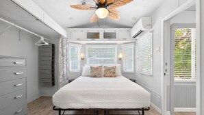 Une chambre à coucher comprenant un lit, un ventilateur de plafond, une armoire et une fenêtre avec des stores.