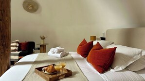 Ein Hotelzimmer mit einem Bett, Kissen, einem Nachttisch mit Lampe, einer Ablage mit Croissants und Saft sowie einer Wandleuchte.