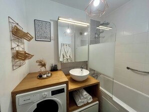 Ein modernes Badezimmer mit einem Holzkosmetikschrank, einem weißen Waschbecken, einem Spiegel, einer Dusche und einer integrierten Waschmaschine.