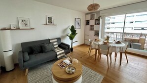 En moderne stue med en grå sofa, et rundt sofabord og et spiseområde med hvid dug.