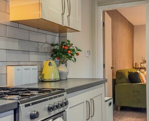 A kitchen with a stove, cabinets, a plant, and a coffee maker.