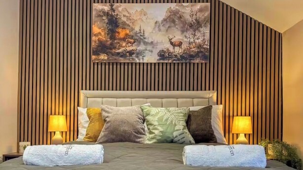 A bed with a quilted cover, two pillows, and a headboard with a painting above it. - Forest Inspired Home! Near M1 and Superb Locations (Nottingham)
