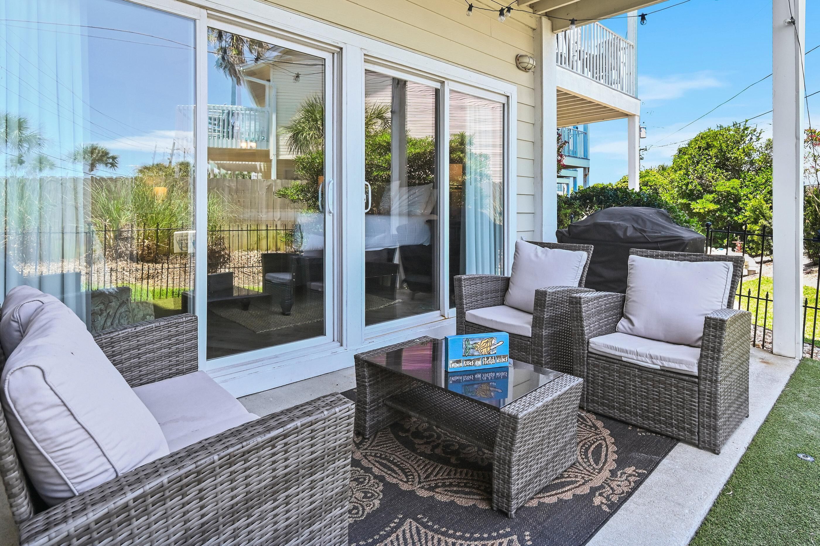 A covered patio with wicker furniture, a glass door leading to a balcony, and a barbecue grill.