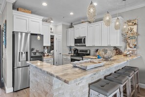 A modern kitchen with white cabinetry, stainless steel appliances, a marble island, and pendant lighting. - Beach Pointe 102- The Salty Seahorse (Destin)