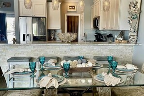 A modern kitchen with white cabinets, a glass dining table, and decorative lighting. - Beach Pointe 102- The Salty Seahorse (Destin)