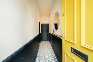 Un couloir étroit avec un sol à motifs noir et blanc, une porte noire au fond et une porte jaune sur la droite.