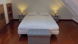 A bedroom with a large bed, two bedside tables with lamps, a bench at the foot of the bed, and wooden flooring. - KaZa Bel'Vi By La Manoshra (Capesterre de Marie-Galante)