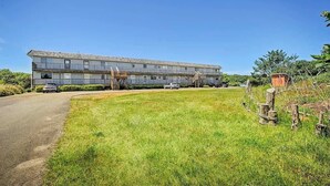 A multi-story building with a flat roof, a parking area, and a grassy lawn. - Ocean Surf Condo | Queen Bed | Sleeps 4 | Unit 207 (Ocean Shores)