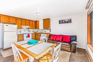Una cocina compacta con armarios de madera, un refrigerador blanco y una zona de comedor con mesa y sillas.