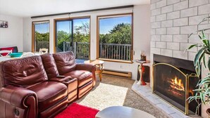 A living room with a leather sofa, a fireplace, and large windows. - Ocean Surf Condo | Queen Bed | Sleeps 4 | Unit 207 (Ocean Shores)