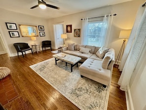 A living room with a sofa, two armchairs, a coffee table, a rug, and a ceiling fan.