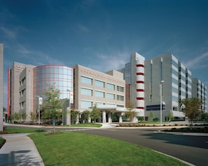 A modern hospital building with a curved glass facade, multiple entry points, and a landscaped entrance area.