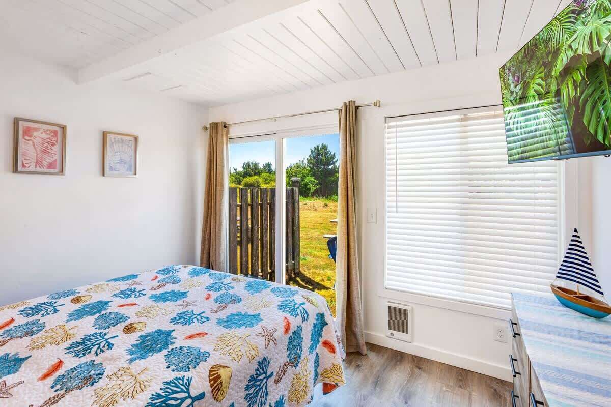 A bedroom with a bed, a window with blinds, a view of the outdoors, and a sailboat model on a table.