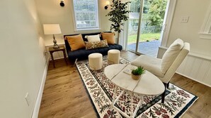 Een woonkamer met een bank, poefjes, een ronde tafel, een lamp en een kamerplant.