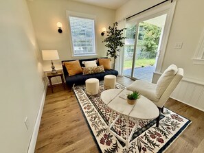 A living room with a sofa, ottomans, a round table, a lamp, and a potted plant.
