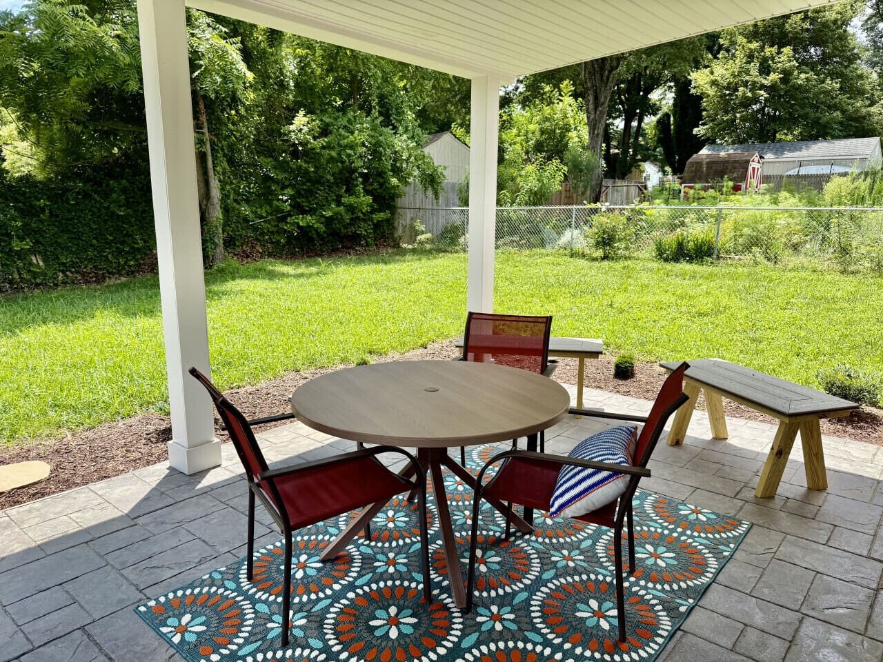 Um alpendre coberto com uma mesa redonda e cadeiras, um banco e um tapete decorativo.