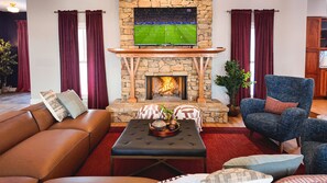 A living room with a stone fireplace, a television mounted above it, leather sofas, and a blue armchair.