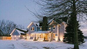 A two-story house with a snow-covered driveway and a large tree in the foreground. - Sleep 30, Near Grand Park, Golf Sim, Sauna, Hottub (Westfield)