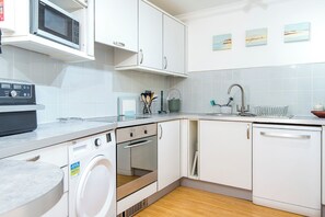 A modern kitchen with white cabinetry, a built-in oven, a washing machine, a microwave, and a sink with a faucet. - Larus, Holiday Apartment Smoke House Quay, Milford Marina, Sleeps 4, 2 bedrooms,  bathrooms (Milford Haven)