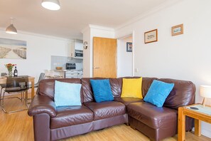 A brown leather sofa with colorful cushions, a wooden side table, and a dining area with a chair and table. - Larus, Holiday Apartment Smoke House Quay, Milford Marina, Sleeps 4, 2 bedrooms,  bathrooms (Milford Haven)