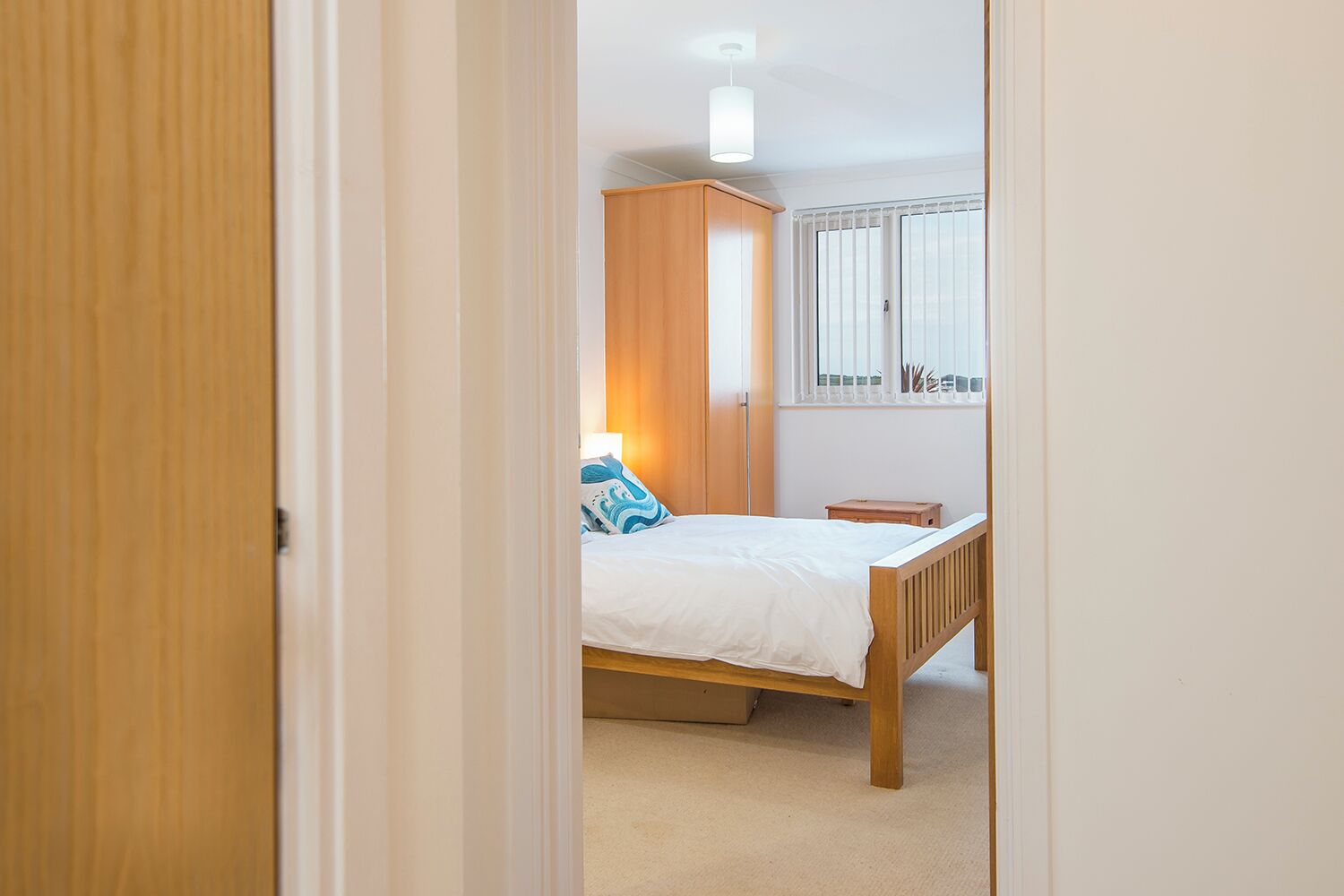 A bedroom with a bed, a wardrobe, a bedside table, and a window with blinds.