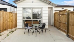A patio with a table and chairs, a sliding glass door, and wooden fences. - Room-1 Spacious Bedroom Available (Papakura)