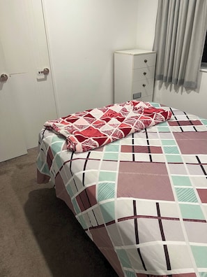 Un dormitorio con cama, mesita de noche, armario y ventana con cortinas.