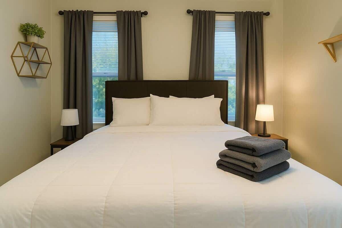 A neatly made bed with white linens, a headboard, and two bedside lamps.