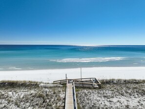 A beach with a wooden boardwalk leading to the water, sandy dunes, and a clear blue sky. - Aegean 220 (Destin)