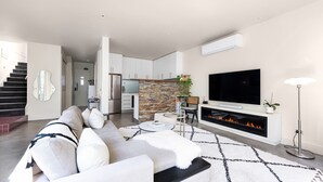 Ein modernes Wohnzimmer mit Sofa, Kamin, Fernseher und einer Küche im Hintergrund.