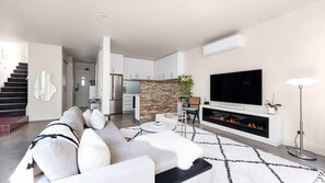 Ein modernes Wohnzimmer mit Sofa, Kamin, Fernseher und einer Küche im Hintergrund.