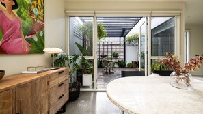 Ein modernes Interieur mit einem Holzkabinett, einem Tisch mit einer Vase und Blick auf eine Außenpatio-Terrasse mit Pflanzen und einer Sitzgruppe.