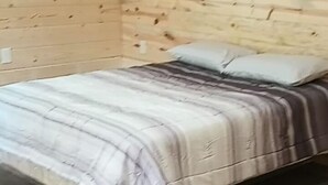 Puupaneeliseinäinen huone, jossa on sänky, seinällä taulu ja lattialla laatat.