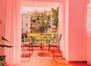 Un balcón con mobiliario exterior, piso de baldosas y vista a edificios cercanos.