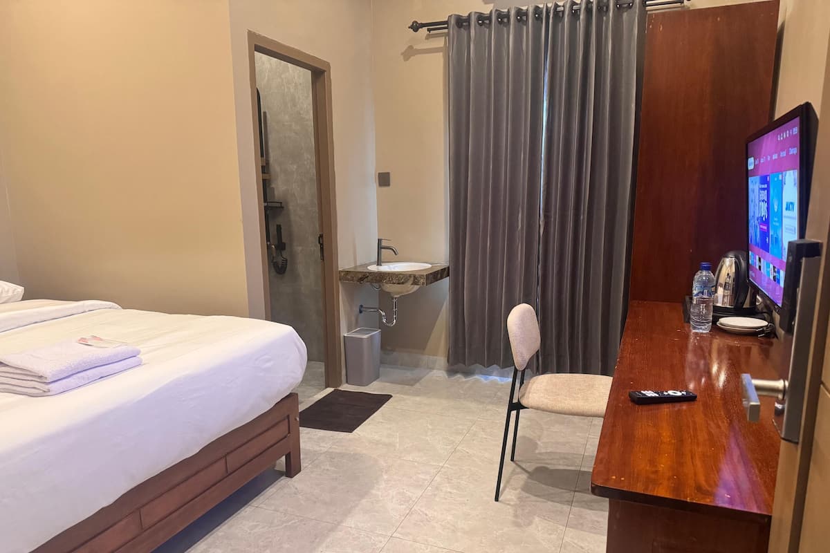 A hotel room with a bed, a desk with a computer, a chair, a sink, and a door.