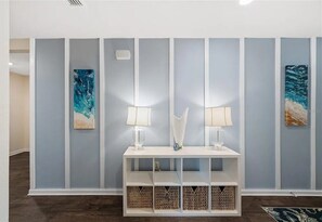A hallway with a white console table, two lamps, and three wall-mounted paintings. - Modern Coastal Retreat w/ Pergola & Fenced Yard (Palm Coast)